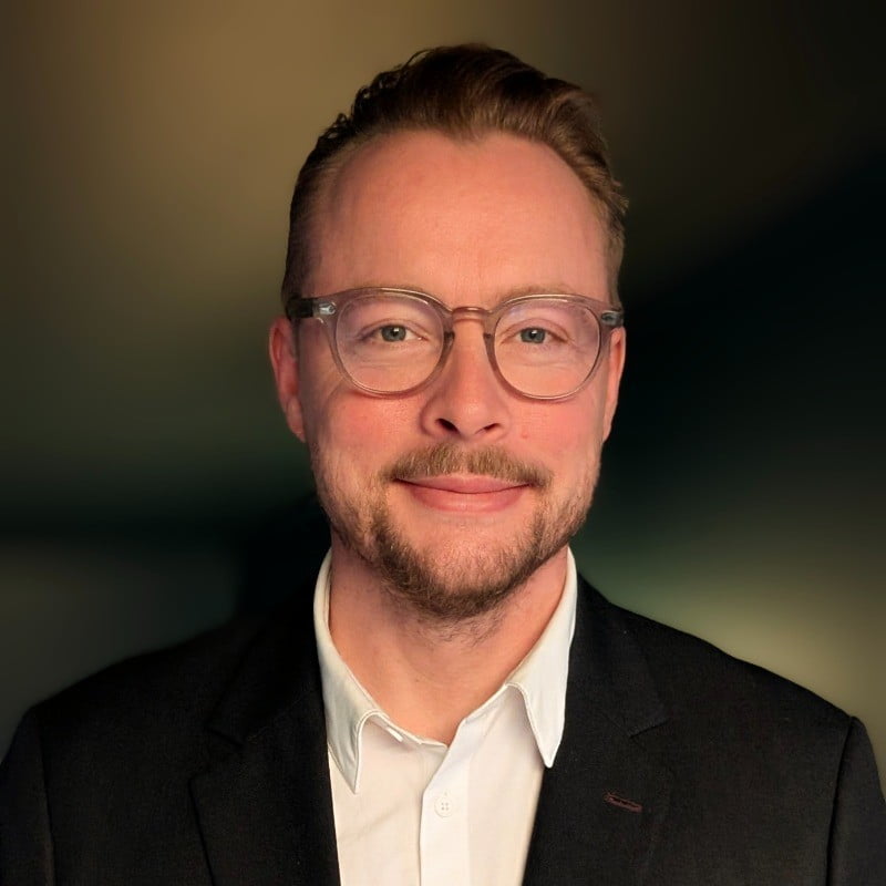 Frederik Nicolaisen, Sikkerhetssjef i Eika, smiler mot kamera i portrett med mørk bakgrunn.